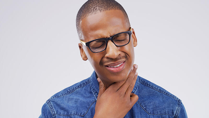 Black man, sore throat and virus in pain, allergies or bacteria against a white studio background. Sick African male person touching neck from cough, allergy or flu of cold, illness or infection