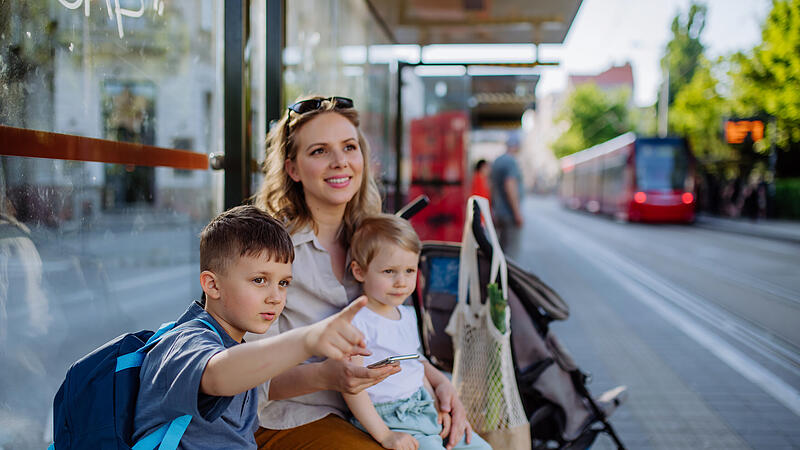 Young mother with little kids waiting on bus stop in city.