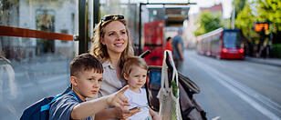 Young mother with little kids waiting on bus stop in city.