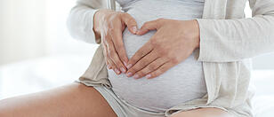 close up of pregnant woman making heart gesture