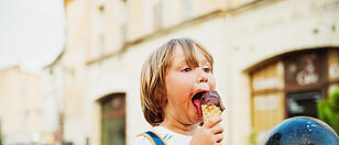 Cute little boy eating chocolate ice cream outdoors, wearing backpack, travel with kids