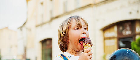 Cute little boy eating chocolate ice cream outdoors, wearing backpack, travel with kids