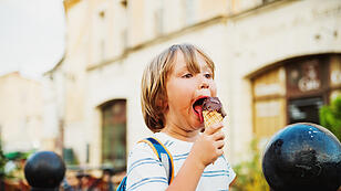 Cute little boy eating chocolate ice cream outdoors, wearing backpack, travel with kids