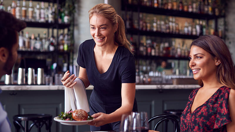 Female Waitress  Serving Food To Romantic Couple Sitting At Restaurant Table
