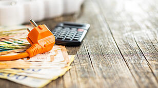 Electric plug, calculator and euro money on wooden table.