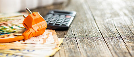 Electric plug, calculator and euro money on wooden table.