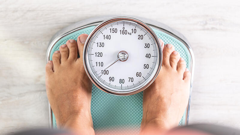 Woman looks down at the number of pounds or kilograms as she stands on a weighing scale