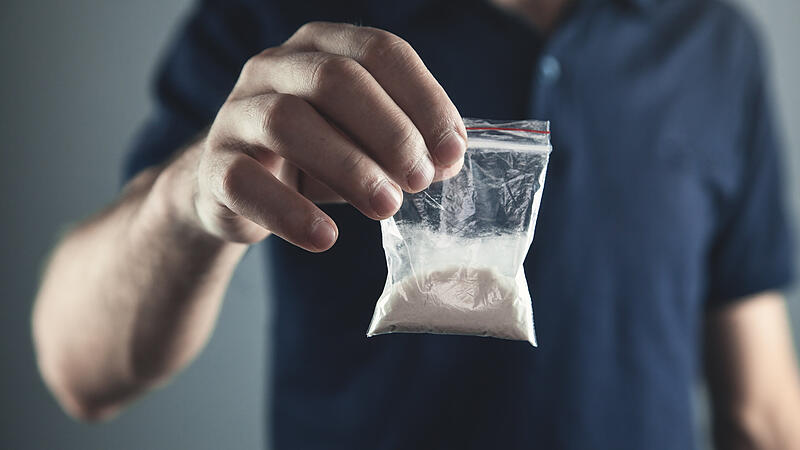 Drug dealer holding plastic packet with cocaine powder.