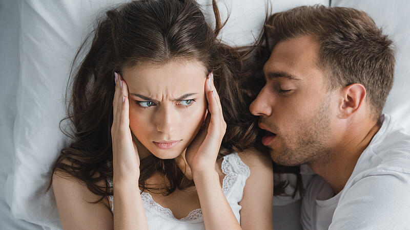 top view of young woman with headache looking at husband snoring in bed