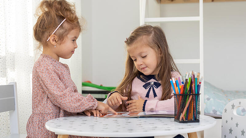 Cute children girls are reading a book in room at home. Two sister girls reading a book and having fun.