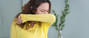 Young woman with face mask sneezing into elbow