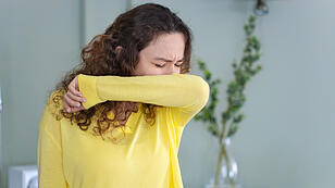 Young woman with face mask sneezing into elbow