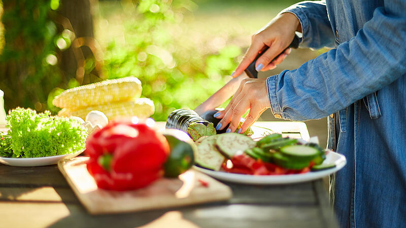 Unrecognizable woman cutting fresh eggplant vegetables on wooden board