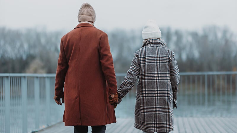 Rear view of senior couple walking near the river, during cold winter day.