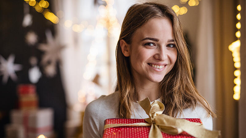 Happy young woman indoors at home at Christmas, holding present.