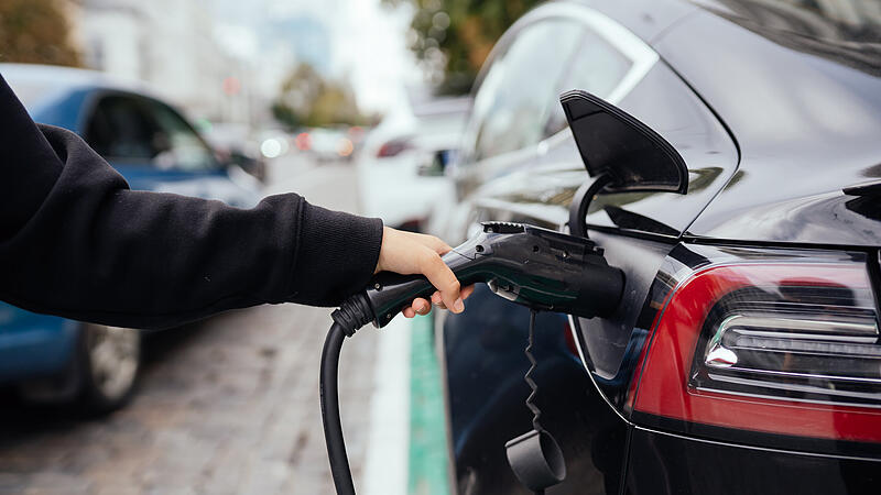 Woman near electric car. Vehicle charged at the charging station.