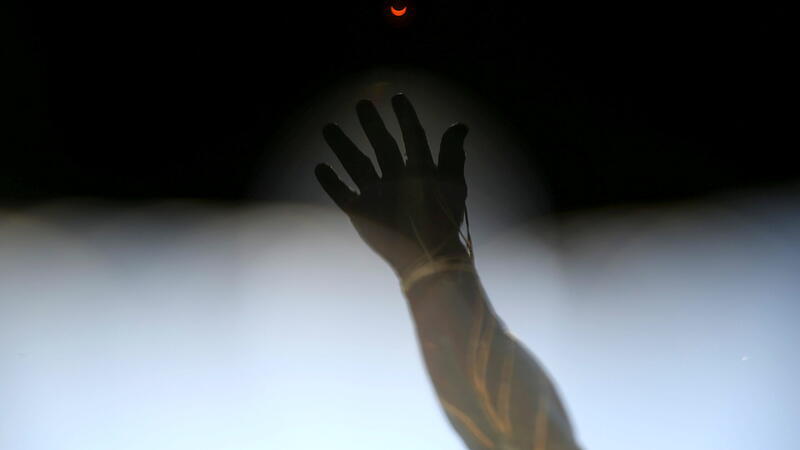 A solar eclipse is seen through filters from special solar glasses in front of a sculpture, in Santiago