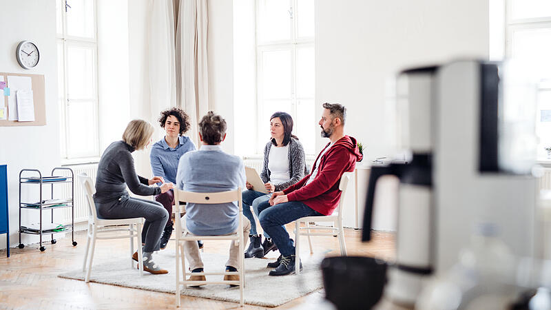 Men and women sitting in a circle during group therapy, talking.