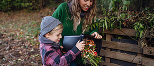 Boy helping mother to put kitchen waste, peel and leftover vegetables scraps into composter in the garden. Concept of composting kitchen biodegradable waste.