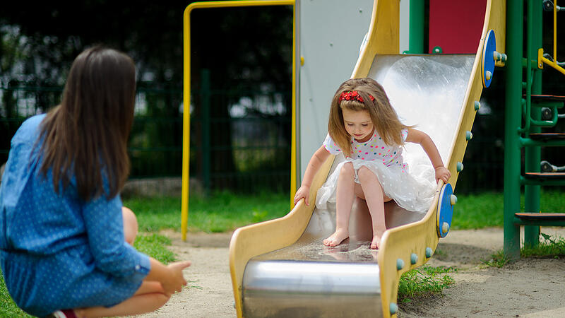 Mom and her little daughter are playing on the playground.