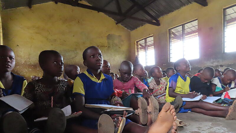 Alltag in Schulen im ländlichen Uganda: Überfüllte Klassen, Schreibblock auf dem Oberschenkel