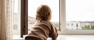 The child climbs to the window, the girl on the window sill rests on the net, the danger of falling. The child is alone at home, can fall out of the window.